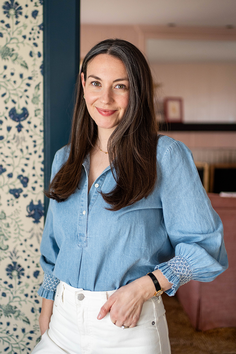 Carly Riordan wearing a chambray shirt leaning against a wall