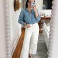 Carly Riordan taking a mirror selfie wearing a chambray shirt and white jeans.